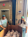 Two people standing next to a large cardboard box filled with wrapped poultry ready for delivery in an indoor setting.